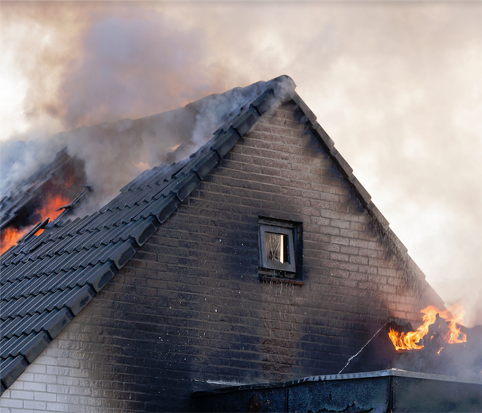 the roof of a house on fire with smoke billowing from the openings